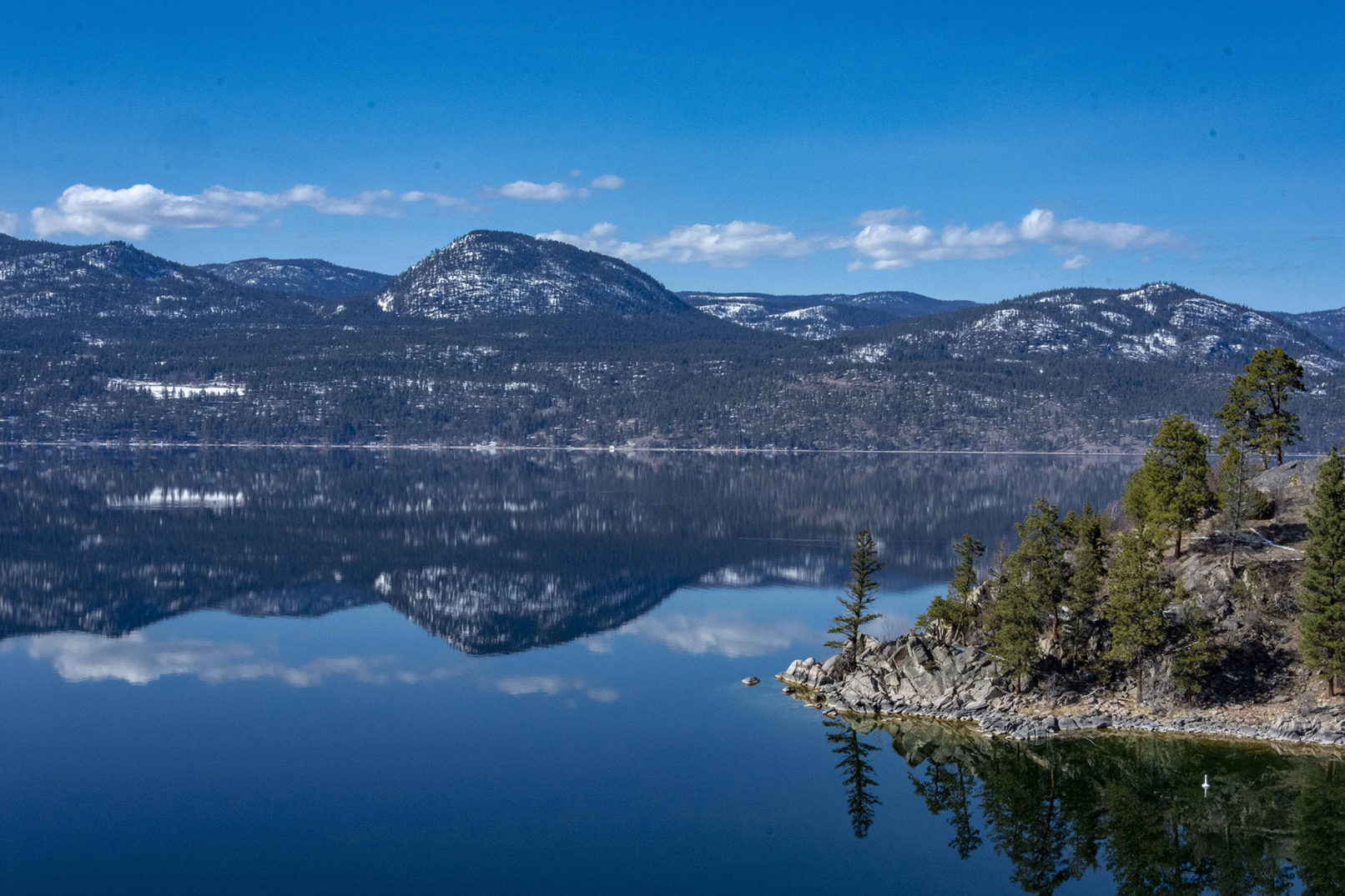 reflections on a lake during a bluebird day with a small island on the extreme right