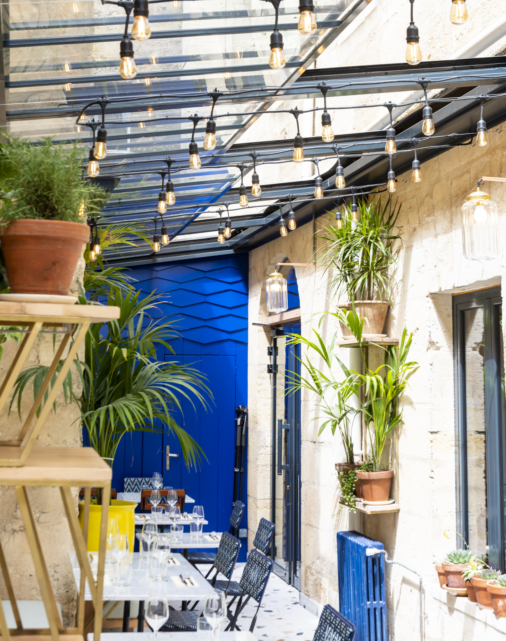 la cour arrière d'un restaurant avec plusieurs pot de plantes vertes, sol marbré et fond bleu