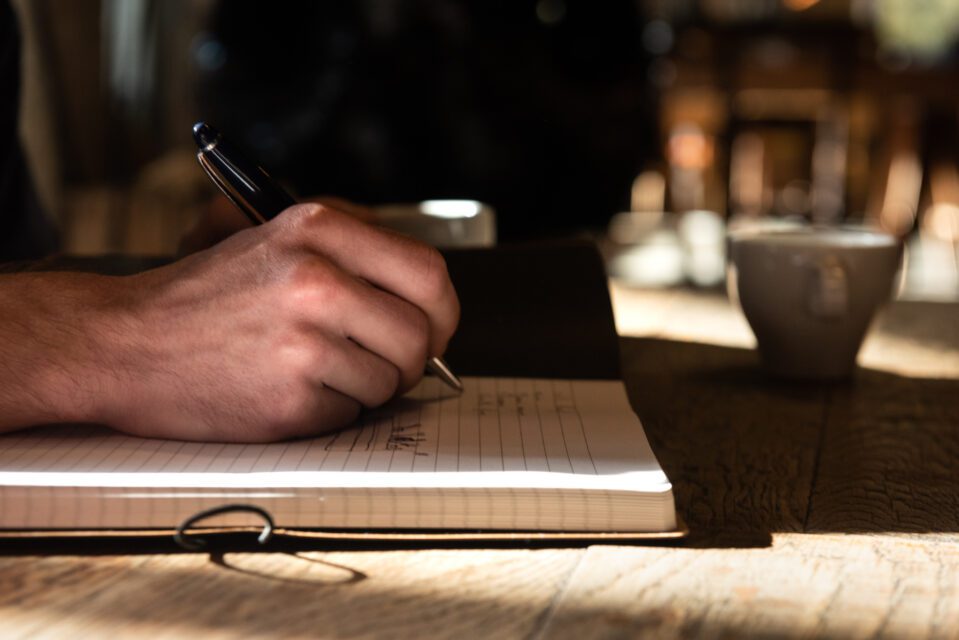 Main tenant un stylo et prenant des notes sur un carnet avec une tasse à côté