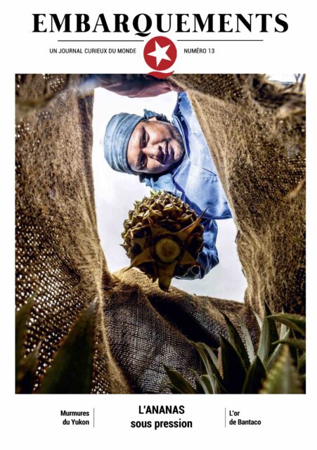 Couverture numéro 13 du journal Embarquements, un homme insert un ananas dans un sac en jute.